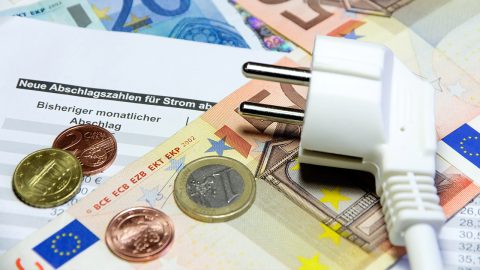 ifi_ Ein weißer Stecker, Euro-Münzen und Geldscheine sind auf einer deutschen Stromrechnung platziert und symbolisieren die Kosten für Energie.
